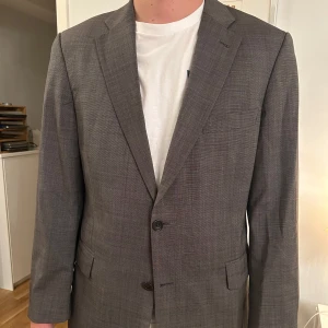 Grå kavaj från Ströms - Snygg grå kavaj från Ströms Göteborg. Perfekt för både formella och semi-formella tillfällen. Kavajen har en klassisk design med två knappar och fickor fram, samt på insidan.