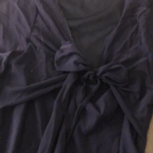 Mörkblå långärmad topp med knytning - Säljer en mörkblå långärmad topp med knytning framtill. Toppen har en v-ringad design och är tillverkad i ett mjukt material. Perfekt för en stilren look🫶🏼
