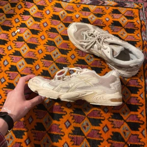 Vita sneakers från Asics - Säljer ett par vita Asics sneakers med snörning. Skorna har en sportig design med synliga detaljer och en bekväm sula. Perfekta för vardagsbruk eller träning. Skick: se bilder, lite smutsiga men inget som inte går och fixa.