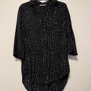 Svart Tunika från Cellbes - Snygg svart tunika från Cellbes. Med vita mönster. Perfekt för en stilren look. Toppen har en rund halsringning och ett lätt fall. 