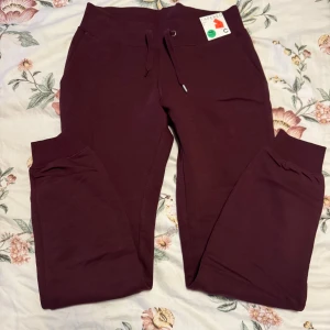 Vinröda mjukisbyxor med snörning - Säljer ett par vinröda mjukisbyxor i storlek S. Byxorna har en bekväm tapered passform och är utrustade med snörning i midjan för justerbar passform. Perfekta för en avslappnad stil.