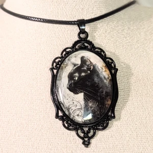 Svart halsband med kattmotiv - Unikt svart halsband med ett stort hänge som har ett konstnärligt kattmotiv. Hänget är ovalt och inramat i en dekorativ svart ram. Kedjan är justerbar med en enkel låsning.Material och märket ospecificerat, därför kategoriserat under 'Övrigt materia, ' inget varumärke '