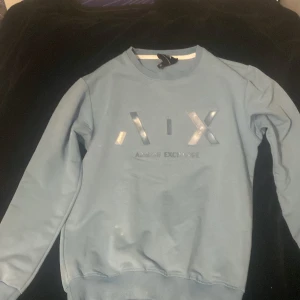 Armani Exchange baby blue tröja - Snygg baby blue tröja från Armani Exchange med logotypen A|X i  på framsidan. Tröjan har rund hals och långa ärmar, perfekt för en stilren look. Passar bra till jeans. den har minskats i tvätten så den kanske sitter bra på  någon som är 160 cm lång och smal