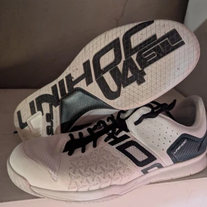 Vita innebandyskor från Unihoc - Snygga vita innebandyskor från Unihoc med svarta detaljer och snörning. Skorna har en mönstrad sula för bra grepp och är perfekta för inomhusaktiviteter.