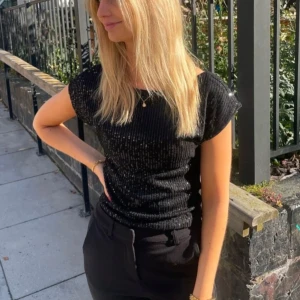 Svart glittrig topp - Snygg svart topp med glittriga paljetter som ger en festlig look. Perfekt för en utekväll eller festlig tillställning. Prislapp kvar och inte använd.