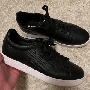 Ea7 Emporio Armani sneakers  - Snygga svarta sneakers från Emporio Armani. Snygg design med logga på sidan. Nypris är ungefär 2000kr. Mit priss 600. Skicket är som nya pga av dem inte är använda någonting. Bara testade 