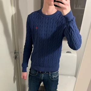 Morris tröja - Säljer en snygg blå kabelstickad tröja från Morris med det klassiska röda logotypen på bröstet. Tröjan har rund hals och långa ärmar. Tröjan är använd och tvättat ett par gånger. Jag är ca 183, men tröjan passar dig mellan 170-180. Hör av dig vid frågor. 