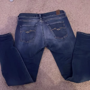 Blå jeans från Replay - Snygga blå jeans från Replay med klassisk femficksdesign och diskreta slitningar. De har en normal passform och är perfekta för en avslappnad stil. Märkeslogga på bakfickan ger en extra touch.
