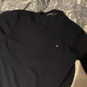 Mörkblå tröja från J.Lindeberg - Snygg mörkblå tröja från J.Lindeberg med diskret logga på bröstet. Perfekt för en stilren look. Tröjan har en klassisk passform och rund halsringning.