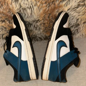 Nike Dunk i blått och vitt - Snygga Nike Dunk sneakers i en stilren kombination av blått, vitt och svart. Skorna har den klassiska Nike-loggan på sidan och en bekväm passform. Perfekta för en sportig look.