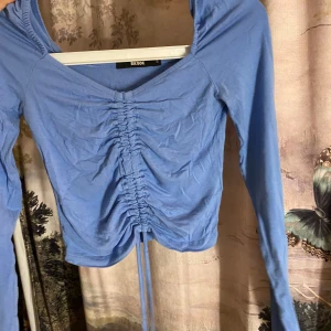 Blå långärmad topp från Bik Bok - Snygg blå långärmad topp från Bik Bok med knytning framtill. Perfekt för en stilren look med en touch av detalj. Toppen har en v-ringad design och är tillverkad i ett mjukt material.