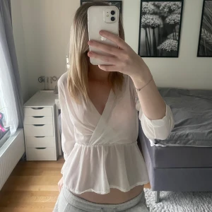 Vit omlottblus från Boohoo - Säljer en elegant vit omlottblus från Boohoo. Blusen har långa ärmar och en vacker volangdetalj i midjan som ger en feminin touch. Perfekt för att klä upp en outfit med stil. 💫