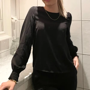 Svart blus med långa ärmar - Elegant svart blus med långa ärmar och rund halsringning. Blusen har en stilren design och är perfekt för en chic look. Den är tillverkad i ett mjukt och bekvämt material.