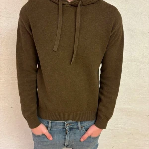 Brun Stickad hoodie från Visual Clothing Project - Säljer en stilren brun stickad hoodie från Visual Clothing Project. Tröjan är stickad och har långa ärmar samt en klassisk huva med dragsko. Perfekt för en avslappnad stil.