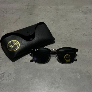 Svarta solglasögon från Ray-Ban - Snygga svarta solglasögon från Ray-Ban med klassisk design och silverdetaljer. De har en stilren look och kommer med ett svart fodral för säker förvaring. 