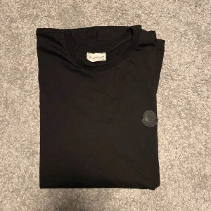 Svart t-shirt från Moncler - Säljer en stilren svart t-shirt från Moncler med deras ikoniska logga på bröstet. T-shirten är kortärmad och gjord i mjuk bomull, perfekt för en avslappnad look. Passar bra till både jeans och shorts. 🖤
