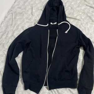 Svart hoodie från Pier One - Säljer en stilren svart hoodie från Pier One med dragkedja och justerbar huva. Perfekt för en avslappnad look. Den har långa ärmar och praktiska fickor framtill. Passar bra till både jeans och joggers.