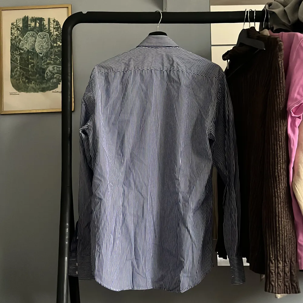 Snygg blå och vit randig skjorta från Morris. Skjortan har långa ärmar och en klassisk krage. Den är broderad med en liten detalj på bröstet och har knappar framtill. Perfekt för en stilren look. Skick 9/10 . Paidat.