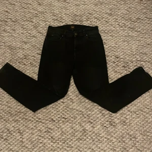 Svarta jeans från Lee - Snygga svarta jeans från Lee med klassisk femficksdesign. De har en knapp och dragkedja framtill. Perfekta för en stilren look.