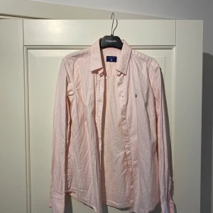 Rosa randig skjorta från GANT - Säljer en stilren rosa randig skjorta från GANT. Skjortan har långa ärmar och knappar framtill. Perfekt för en klassisk och avslappnad look.