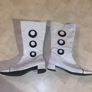 Vita stövlar med svarta detaljer - Snygga vita stövlar med svarta cirkulära detaljer och dragkedja på sidan. De har en låg klack och en spetsig tå, vilket ger dem en retro look.