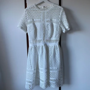 Vit klänning från By Malina - Säljer en elegant vit spetsklänning från By Malina. Klänningen har korta ärmar och en dragkedja i ryggen. Perfekt som studentklänning.
