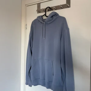 Blå hoodie - Säljer en stilren blå hoodie med justerbar huva och praktisk magficka. Perfekt för en avslappnad look. Passar bra till både jeans och joggers.
