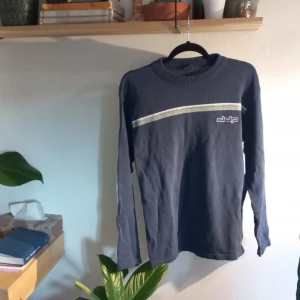 Blå tröja från DDP - Säljer en blå tröja från DDP med en stilren design. Tröjan har en vit och grå rand över bröstet och en rund halsringning. Perfekt för en avslappnad stil.