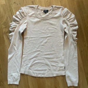 Beige tröja från Bubbleroom - Säljer en stilren beige tröja från Bubbleroom med långa ärmar och rynkade detaljer längs ärmarna. Perfekt för en chic och elegant look. Tröjan är i en mjuk och bekväm kvalitet.