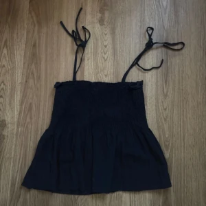 Mörkblå ärmlös topp med knytband - Säljer en mörkblå ärmlös topp med smockdetaljer och knytband vid axlarna. 