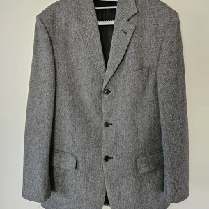 Grå kavaj från KappAhl - Snygg grå kavaj från KappAhl i ullblandning. Kavajen har ett klassiskt snitt med tre knappar framtill och fickor. Perfekt för en stilren look. Sparsamt använd. Axelmått 47cm Längd 84cm