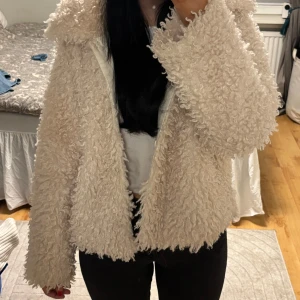 Beige teddyjacka från Kappahl  - Mysig beige teddyjacka från Kappahl med fluffig textur. Jackan har en normal passform och långa ärmar, även fickor. Perfekt för kyliga dagar. Den är tillverkad i syntetmaterial och har en stilren design utan mönster.