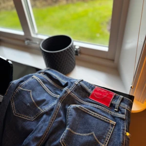Jacob Cohens Jeans w33 - Snygga mörkblå jeans med en iögonfallande röd etikett på baksidan. Klassisk femficksdesign med kontrastsömmar och knappgylf. Perfekta för en avslappnad stil.