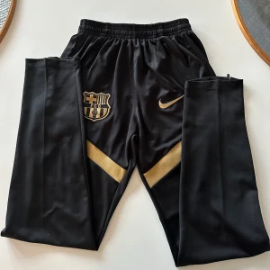 Svarta träningsbyxor FC Barcelona - Snygga svarta träningsbyxor från Nike med FC Barcelona.  är perfekta för sportiga aktiviteter. Ser helt nya du får båda delarna för 400 båda tröjan och byxorna 