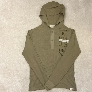 Denim & Supply Ralph Lauren - Hoodie - Säljer en olivgrön hoodie från Denim & Supply Ralph Lauren. Tröjan har långa ärmar och en knappdetalj vid halsen. Den är tillverkad i ett bekvämt bomullsmaterial med tryck på framsidan. Perfekt för en avslappnad stil. Vid minsta fråga eller fundering hör av er🤝