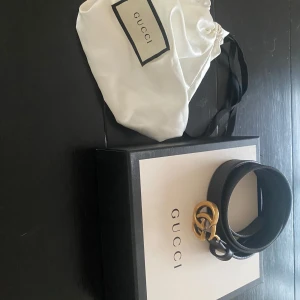 Svart skärp från Gucci - 100cm - Snyggt svart skärp från Gucci i slätt skinn med en ikonisk dubbel G-spänne i antik mässing. Skärpet är 2 cm brett och tillverkat i Italien. Perfekt för att ge din outfit en lyxig touch. Nypris 4200kr.