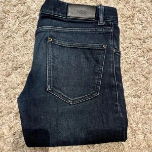 Mörkblå jeans från Bläck - Snygga mörkblå jeans från Bläck med en klassisk femficksdesign. De har en knappgylf och är tillverkade i ett slitstarkt denimtyg. Perfekta för en stilren look. Storlek 48 = S/M