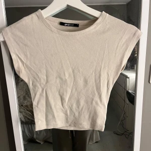 Beige croppad topp från Gina Tricot - Säljer en stilren beige croppad topp från Gina Tricot. Toppen är ärmlös och har en rund halsringning, perfekt för en avslappnad look. Passar bra till både jeans och kjol. Hör av dig vid intresse!
