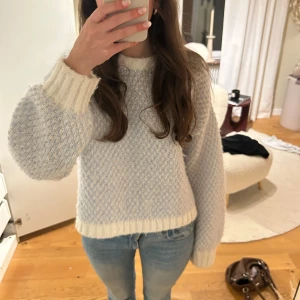 Vit och ljusblå stickad tröja - Mysig stickad tröja i vit och ljusblå nyans. Tröjan har en normal passform med långa ärmar och ribbade muddar vid ärmslut och nederkant. Perfekt för kyligare dagar.