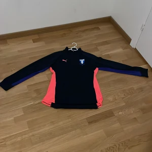 Svart och rosa långärmad tröja från Puma prislapp kan diskuteras - Säljer en svart långärmad tröja från Puma med rosa och blå detaljer. Perfekt för sportiga aktiviteter. Tröjan har en smidig passform och är tillverkad i ett syntetmaterial för optimal komfort.