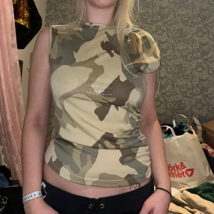 Camouflagefärgad ärmlös topp - Säljer en cool ärmlös topp med camouflage-mönster i beige, brunt och grönt. Med lite andra detaljer. 