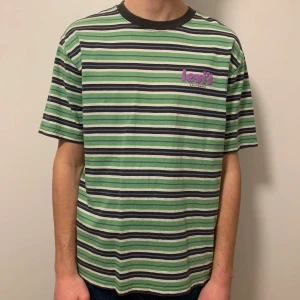 Randig t-shirt från Levi's - Säljer en randig t-shirt från Levi's i grönt, svart och vitt. T-shirten har korta ärmar och en normal passform. Perfekt för en avslappnad stil.