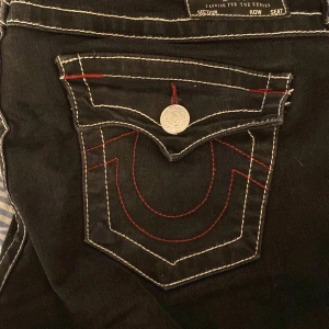 Svarta jeans från True Religion - Snygga svarta jeans från True Religion med röda och vita sömmar. Modellen är Joey med låg midja och fina bakfickor de är bootcut