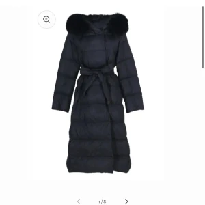 Fur Stocholm Svart dunjacka med pälsdetalj - Snygg och lång svart dunjacka med pälsdetalj på huvan. Jackan har ett bälte i midjan för en figursydd look och långa ärmar. Perfekt för kalla dagar. Nypris 2300kr