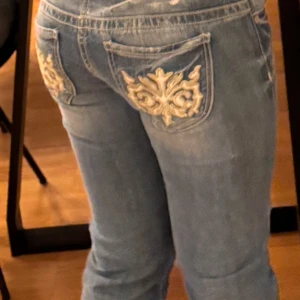 Blå jeans med broderade fickor från Guess - Snygga blå jeans från Guess med unika broderade detaljer på bakfickorna. De har en klassisk femficksdesign och en bekväm passform. Perfekta för att ge din outfit en extra touch av stil.