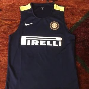 Blå Manchester city fotbollströja finns. i alla storlekar  - Säljer en blå ärmlös fotbollströja från Nike med gula detaljer på axlarna och Pirelli-logga på framsidan. Perfekt för träning eller sommarens fotbollsmatcher. Tröjan har en rund halsringning och klubbemblem på bröstet.