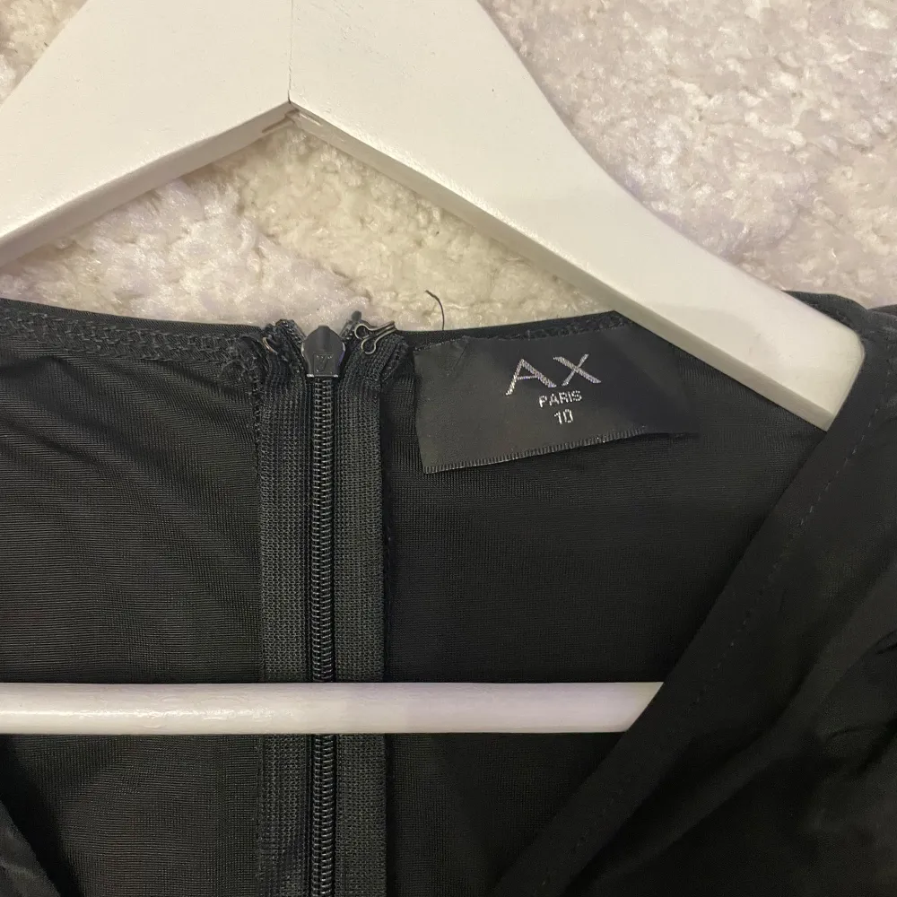 Elegant svart omlottklänning från AX Paris med v-ringning och långa ärmar. Klänningen har en smickrande rynkad design och dragkedja i ryggen. Perfekt för en stilfull kväll.. Mekot.
