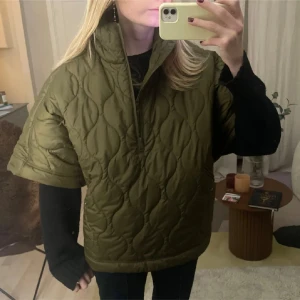 Olivgrön quiltad cape - Säljer denna eftertraktade olivgröna quiltade jacka med korta ärmar och dragkedja framtill. Storlek xs men passar xs-L