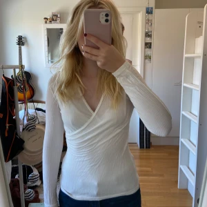 Vit omlottopp - Säljer en superfin vit omlottopp med långa ärmar. Den är perfekt för både vardag och fest och har en v-ringad design. Materialet är och stretchigt, vilket gör den bekväm att bära. Knappt använd, i bra skick förutom att den har en lös tråd i ena armen