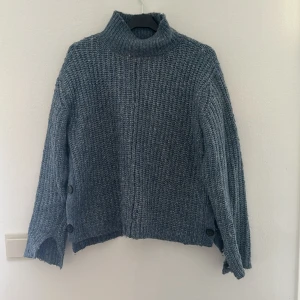 Grå stickad tröja med knappar - Säljer en mysig blå stickad tröja med hög krage. Tröjan har långa ärmar och snygga knappar på sidan som ger en extra detalj. Perfekt för kyliga höst- och vinterdagar. Passar både till vardags och lite finare tillfällen💕knappt använd fortfarande i fint skick!